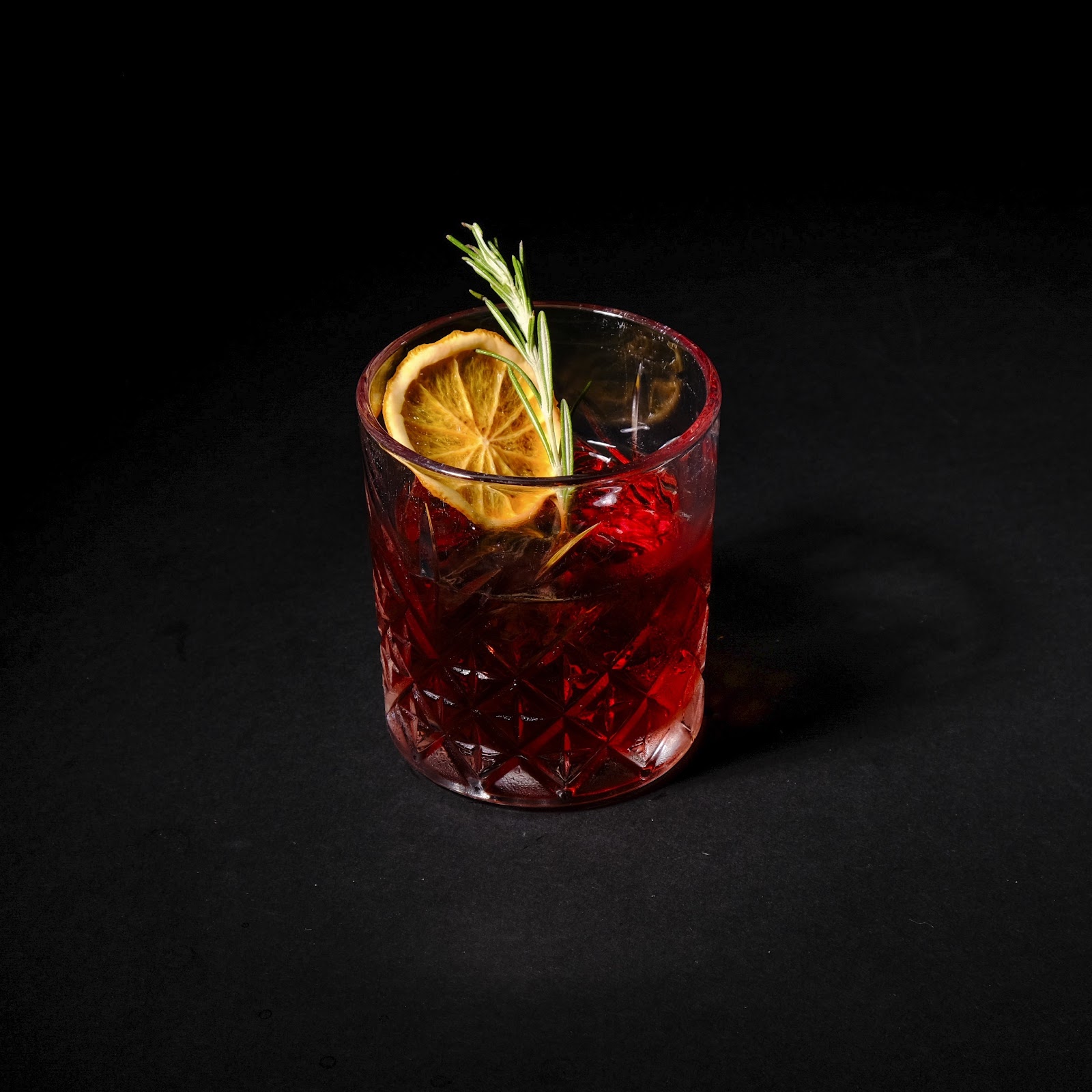 Cocktail rouge grenat en verre taillé avec orange séchée et romarin